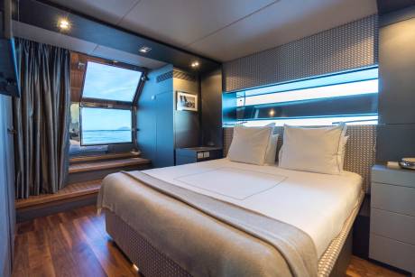 A luxurious bedroom with a neatly made bed in the foreground and an open doorway leading to a deck with a view of the ocean in the background.