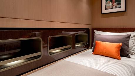 A neatly made bed with orange and gray pillows sits in the foreground, while a framed picture hangs on the wood-paneled wall in the background.
