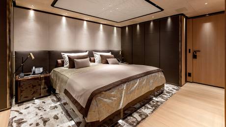A luxurious bedroom with a large bed in the foreground and dark wood paneling and a door in the background.