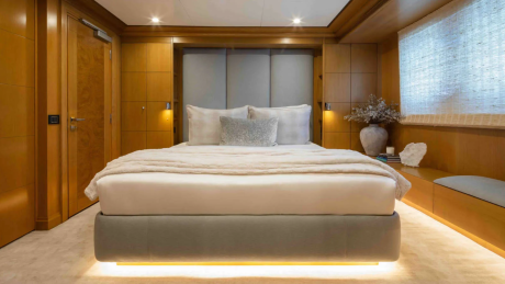 A luxurious bedroom with a plush bed in the foreground and warm wood paneling and a window with blinds in the background.