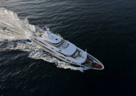 A luxurious white yacht cruises through dark, rippling water, leaving a foamy wake behind it.