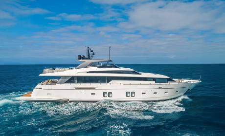 A sleek white yacht cruises through choppy blue waters under a bright, cloudy sky.