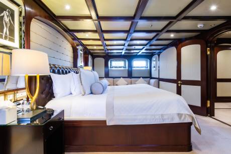 A luxurious bedroom with a large bed in the foreground and a seating area with windows in the background.