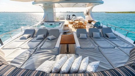 Plush lounge chairs and a hot tub fill the foreground of a luxurious yacht, while the turquoise ocean and distant coastline stretch across the background.