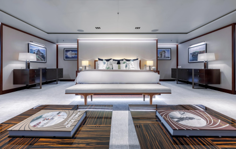 A luxurious bedroom with a large bed and artwork in the background is framed by two wooden tables with books in the foreground.