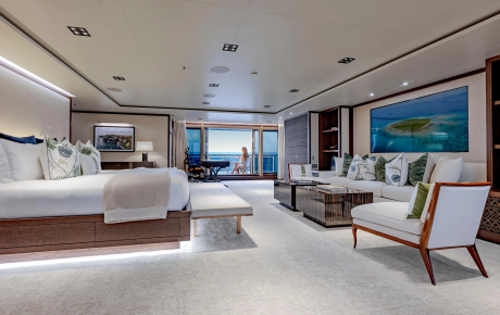 A luxurious bedroom with a large bed in the foreground opens to a balcony with ocean views in the background.