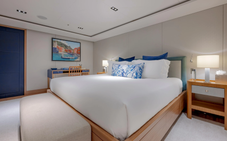 A luxurious bedroom with a large white bed in the foreground and a desk with a painting on the wall in the background.