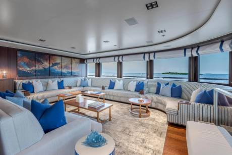 A spacious, modern yacht lounge with plush seating and ocean views is in the background, while a contemporary coffee table arrangement sits in the foreground.