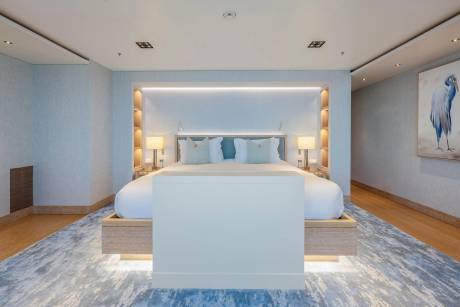 A modern bedroom with a large bed and a white screen in the foreground, and a painting of a bird on the wall in the background.