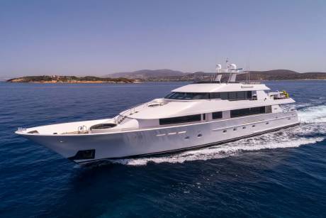 A large white yacht cruises through calm blue water with a distant, hilly coastline under a clear sky.
