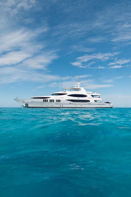 A large white yacht floats on turquoise water under a bright blue sky with scattered clouds.