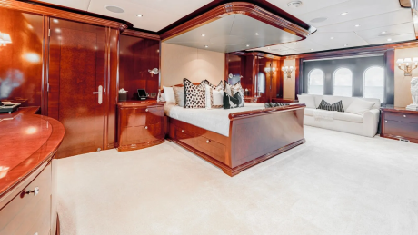 A luxurious bedroom with a large bed and plush carpet in the foreground, and a seating area with a sofa and arched windows in the background.