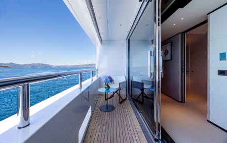 A small table with a floral arrangement sits on a yacht's deck overlooking the ocean and distant hills.