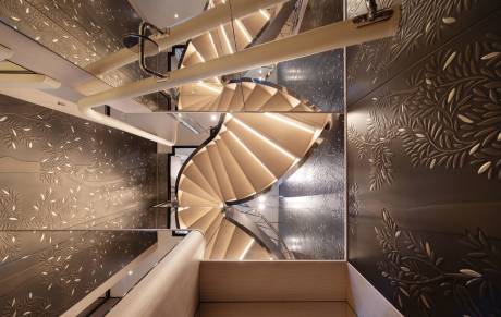 A modern spiral staircase with illuminated treads ascends through a space with intricately patterned walls.