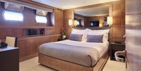A luxurious bedroom with a large bed in the foreground and a mirrored wall with a television in the background.
