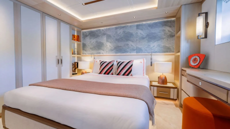 A luxurious bedroom with a neatly made bed in the foreground and a modern vanity and closet in the background.