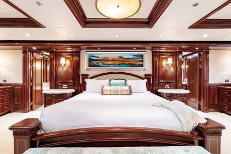 A luxurious yacht bedroom with a large white bed in the foreground and ornate wooden paneling and doorways in the background.