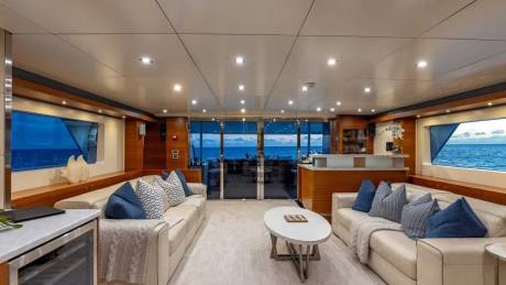 A luxurious yacht interior with plush sofas and a coffee table in the foreground, and a stunning ocean view through large windows in the background.