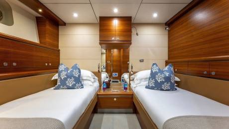 Two neatly made twin beds with blue coral-patterned pillows are in the foreground, while the background features polished wood paneling and cabinetry.