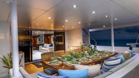 A beautifully set dining table on a yacht's deck is in the foreground, with the ocean and a twilight sky visible in the background.