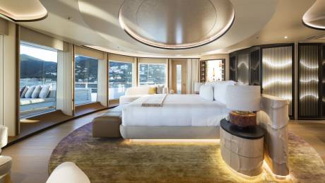 A luxurious bedroom with a large bed in the foreground and a scenic view of a bay with boats and hills in the background.
