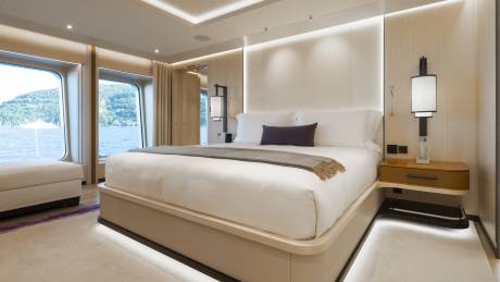 A luxurious bedroom with a large bed in the foreground and a scenic view of water and trees through the windows in the background.