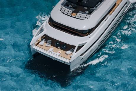 A sleek white catamaran glides through turquoise waters, leaving a foamy wake behind it.