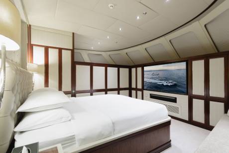 A luxurious bedroom with a large, neatly made bed in the foreground and a large television displaying a boat on the ocean in the background.
