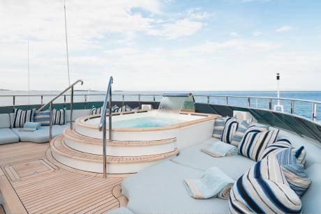 A luxurious yacht's sundeck features a bubbling jacuzzi with a waterfall in the foreground, while the background shows a calm blue ocean under a cloudy sky.