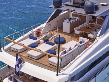 A luxurious yacht deck with lounge chairs and a dining area is anchored in clear blue water.