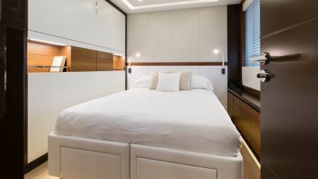A neatly made white bed with pillows dominates the foreground, while the background reveals a modern cabin with wooden accents and a window.