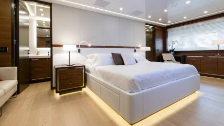 A luxurious bedroom with a large white bed in the foreground and a modern bathroom and desk area in the background.