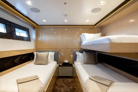 Two twin beds with neatly made white linens and brown accent pillows are in the foreground, while a bunk bed with white linens and a brown accent pillow is in the background, all within a luxuriously appointed cabin.