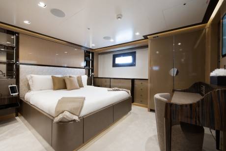 A luxurious bedroom with a large bed in the foreground and a desk and wardrobe in the background.