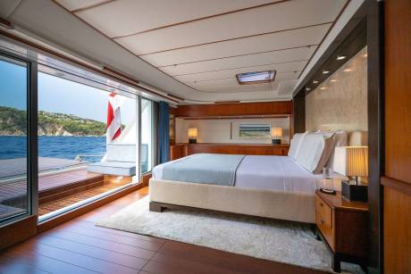 A luxurious bedroom with a large bed and a view of the ocean and a green coastline through a sliding glass door.