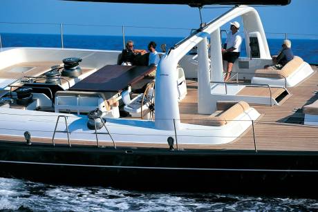 Four people relax on the deck of a large sailboat with the blue ocean stretching out behind them.