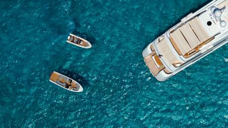 A large white yacht is anchored in the turquoise ocean, with two smaller dinghies nearby.