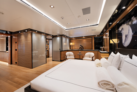 A luxurious bedroom with a large white bed in the foreground and a seating area with two armchairs and a desk in the background.