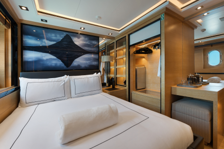 A luxurious bedroom with a large bed in the foreground and a closet and vanity area in the background.