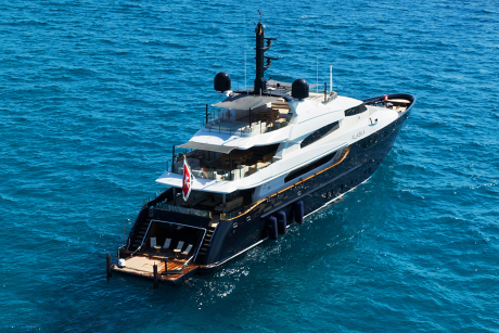 A luxurious dark blue yacht with multiple decks and a wooden swim platform is anchored in clear turquoise water.