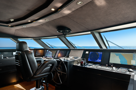 A luxurious yacht's bridge, with a captain's chair in the foreground and a panoramic view of the ocean through large windows in the background.