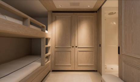 A bunk bed with white mattresses is in the foreground, while a closet with double doors and a shower stall are in the background.