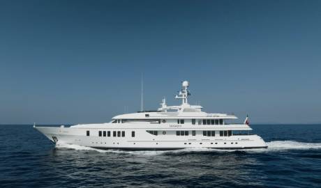 A large white yacht cruises through calm blue water with a clear blue sky in the background.