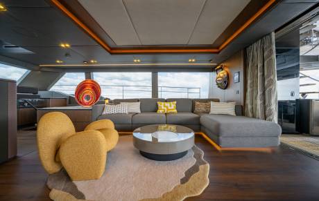 A modern living area with plush yellow armchairs and a sectional sofa in the foreground, and large windows offering a view of the sky and water in the background.