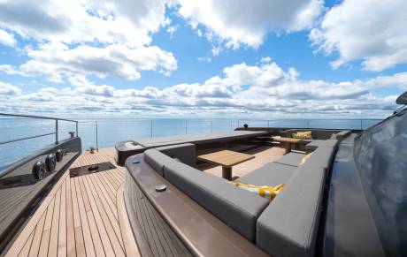 A luxurious yacht deck with plush seating in the foreground overlooks a calm ocean under a cloudy blue sky in the background.