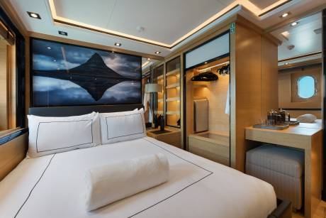 A neatly made bed with white linens occupies the foreground, while a large landscape painting and a built-in wooden wardrobe fill the background.