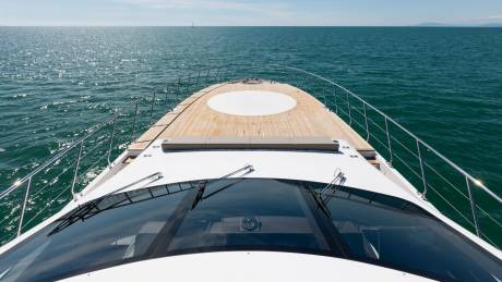 The wooden deck of a white boat leads toward a vast, shimmering blue ocean under a clear sky.