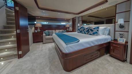 A luxurious bedroom with a large bed and blue accents occupies the foreground, while a seating area and a staircase are visible in the background.