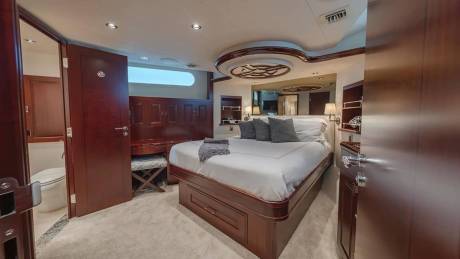 A luxurious bedroom with a large bed and dark wood cabinetry occupies the foreground, while an open door reveals a small bathroom in the background.