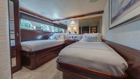 Two twin beds with white linens sit in a luxurious cabin featuring polished wood paneling and small porthole windows in the background.